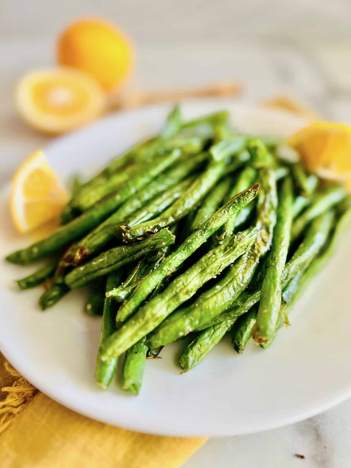 Air Fryer Green Beans Plated portrait with lemon wedges on the side.