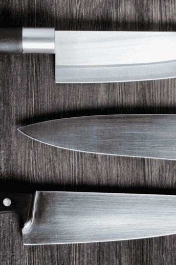 3 Chef knives costing under $100 on a wooden counter top.