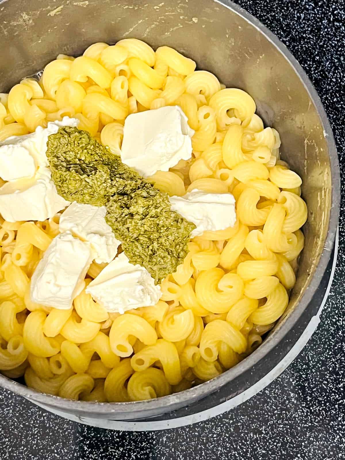 Pot with cooked cavatappi pasta in it and cream cheese and pesto added.