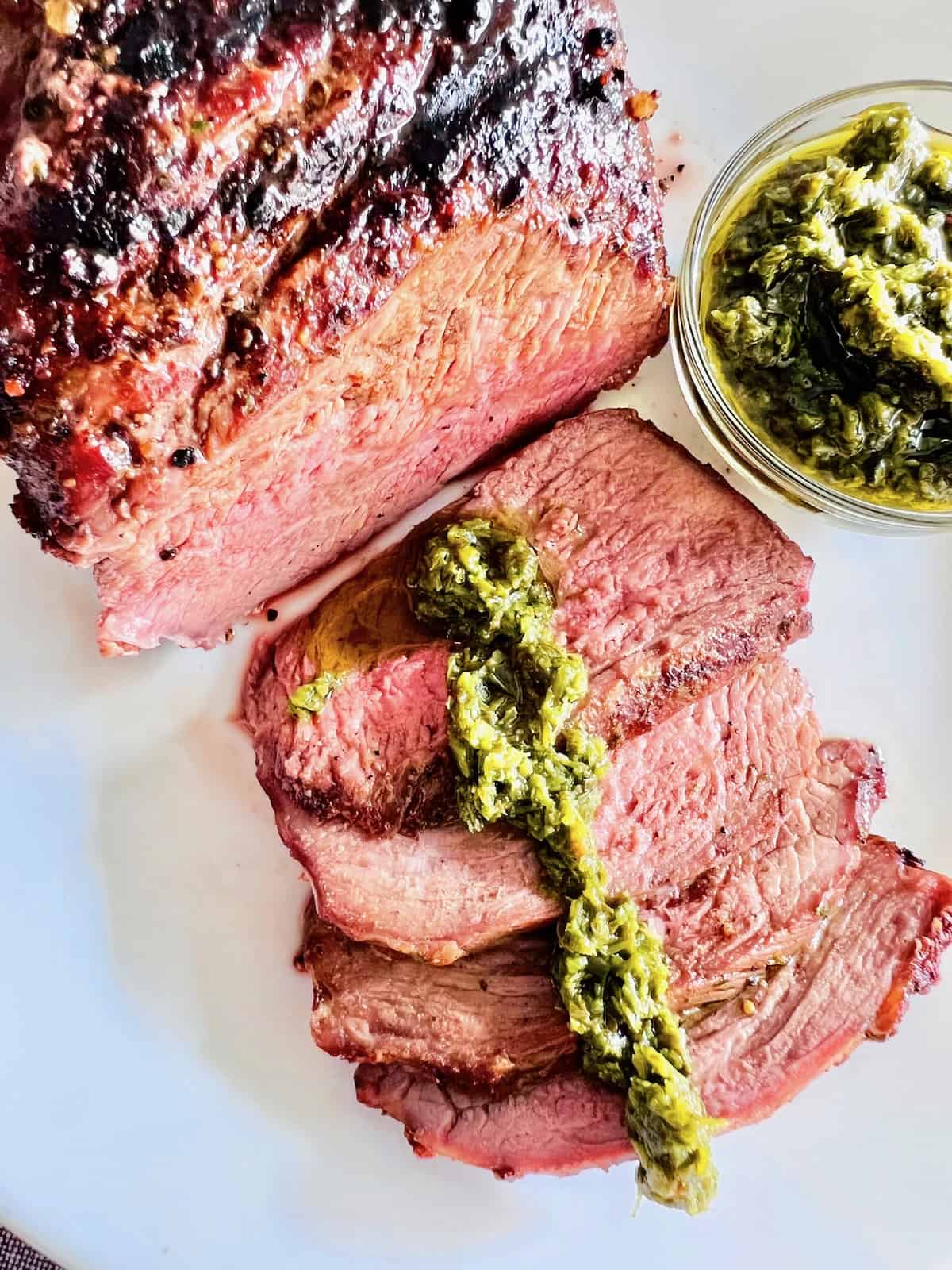 Grilled Tri-Tip Roast overhead closeup cut into a few slices topped with chimichurri.