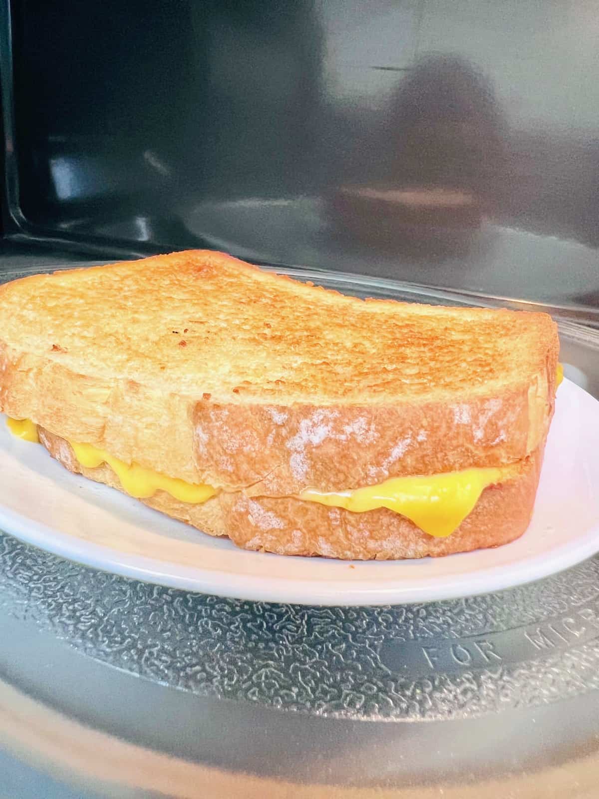 Melted cheddar dripping out of the bread from the plated sandwich in the microwave.