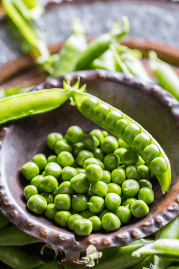 Fresh Spring peas shelled in a bowl and some in their pods still - a great substituet for fava beans.