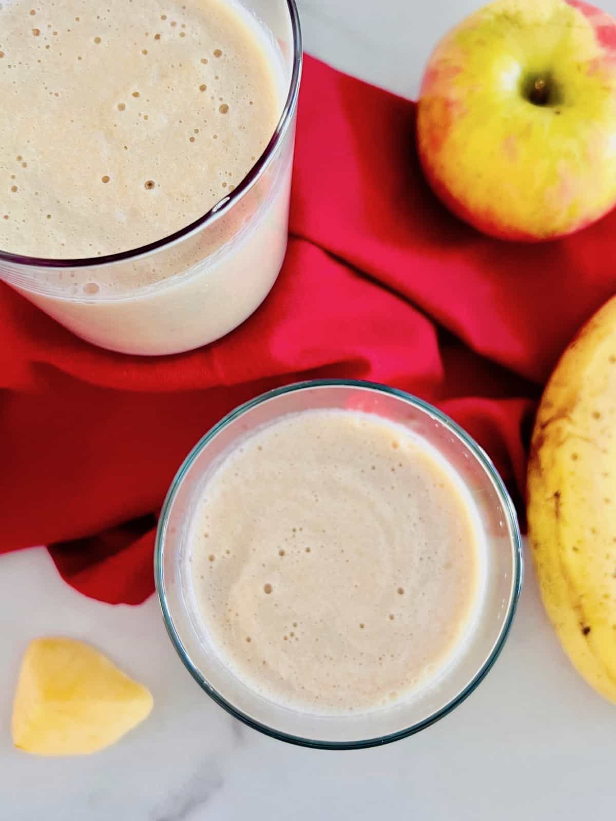 Smoothie in two glasses filled next to apple and banana and red napkin