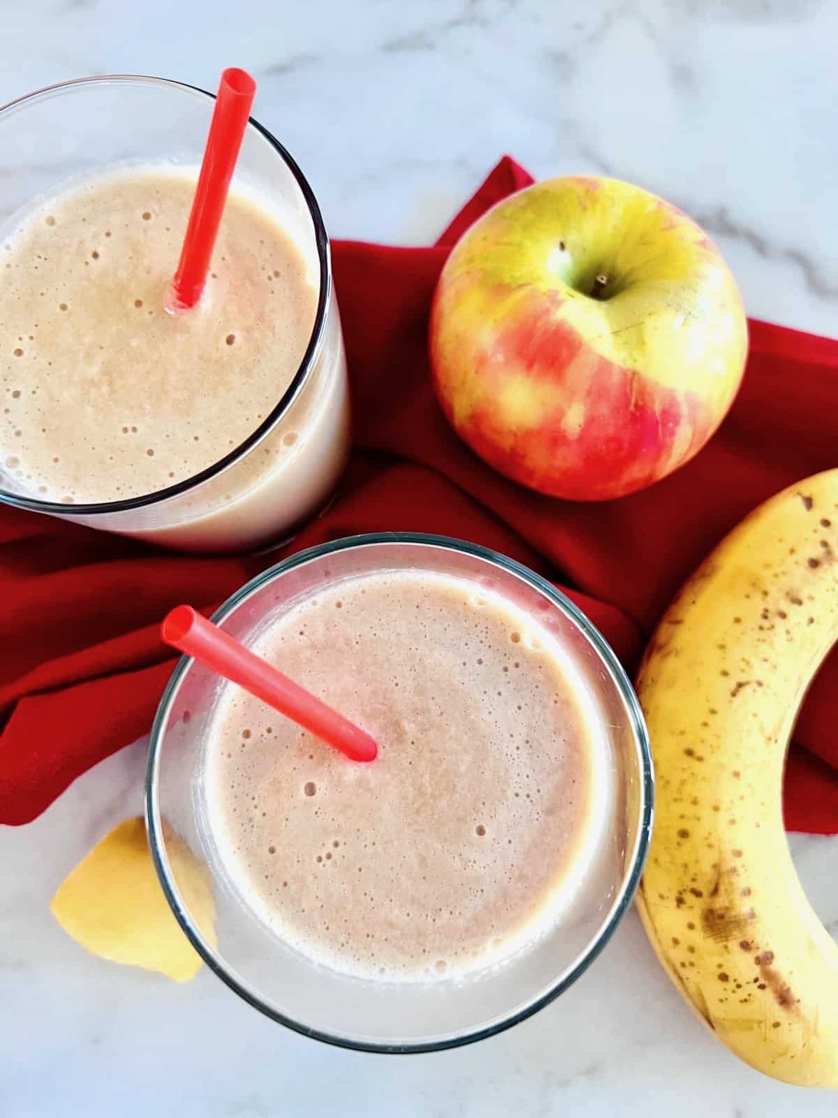 Apple Banana Smoothie two glasses overhead with red straws in them plus apple and banana to the side.