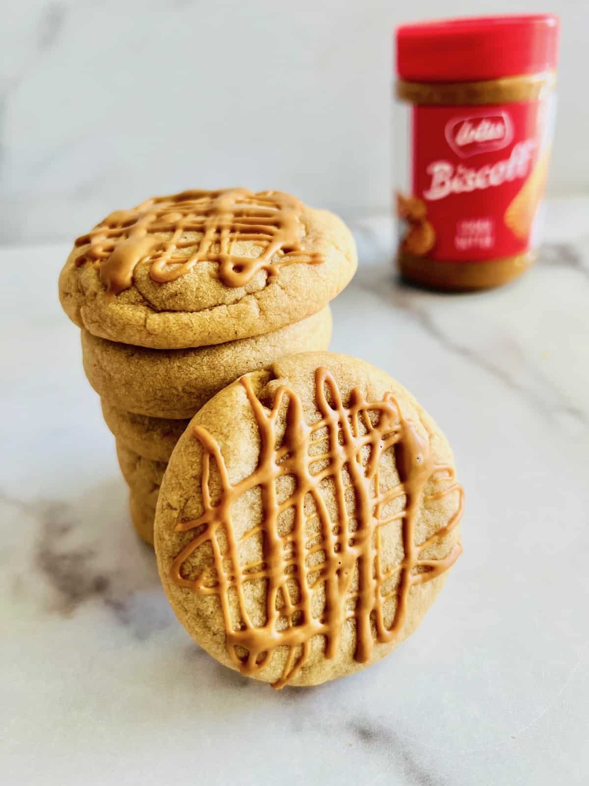 Biscoff Butter Cookies Stacked up with a drizzle topping and Biscoff jar in background.