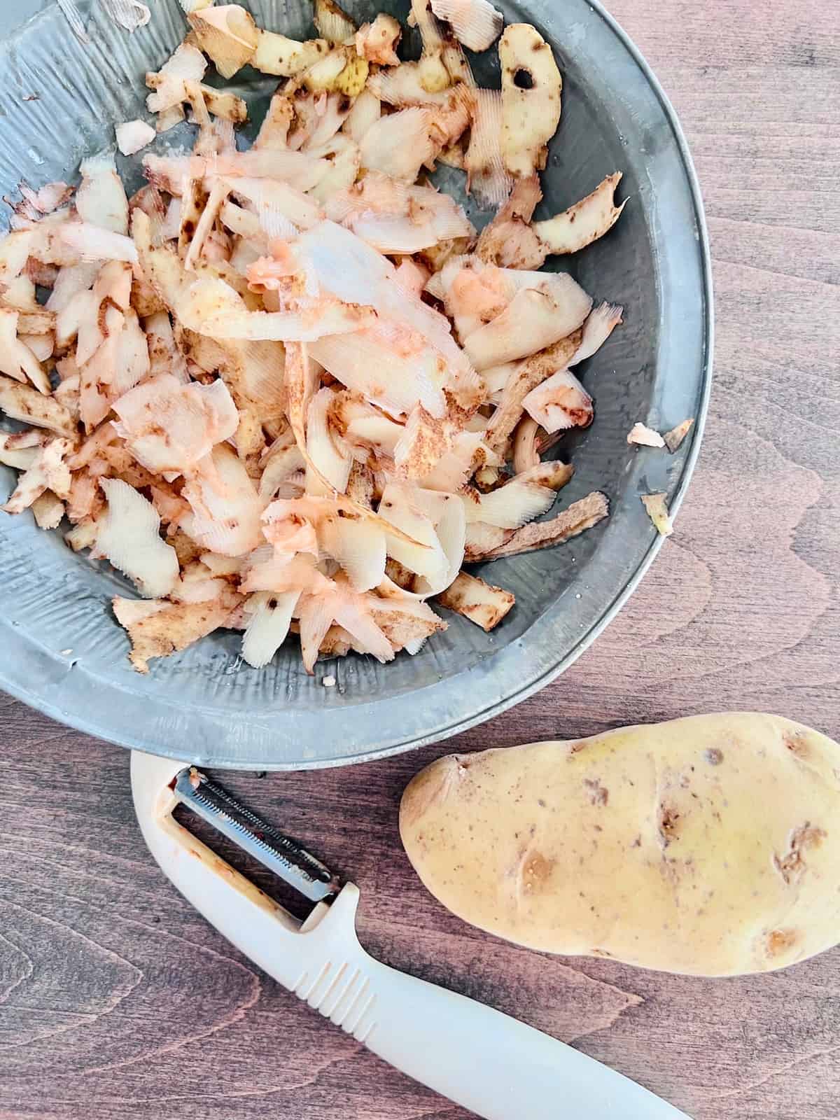 Potato Peels Peels in a pan next to a russet and peeler.