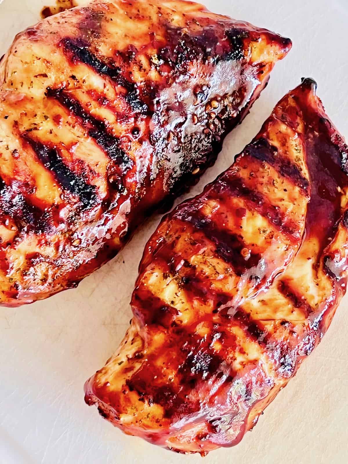 Chicken breasts removed from the grill and resting on a cutting board.