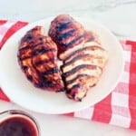 Plated grilled boneless skinless chicken breasts with bbq sauce on top & served on the side.