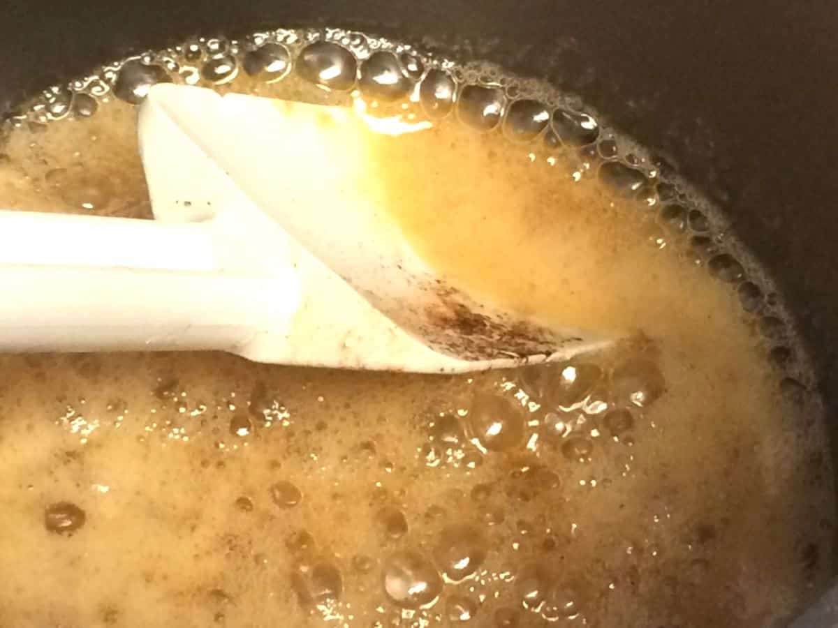 A pot with bubbling peach and sugar simmering to make a sauce with brown sugar and vanilla.