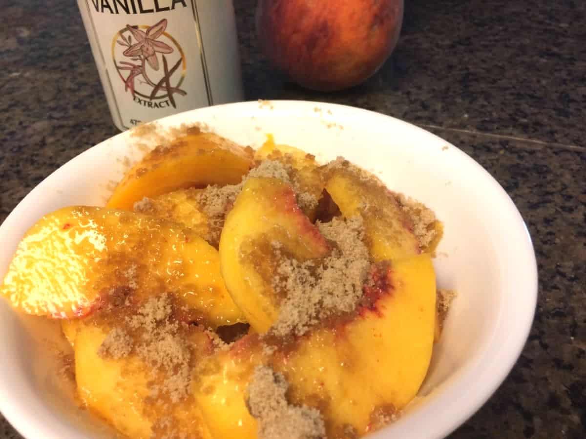 Brown sugar sprinkled over fresh slices of peach in a bowl.