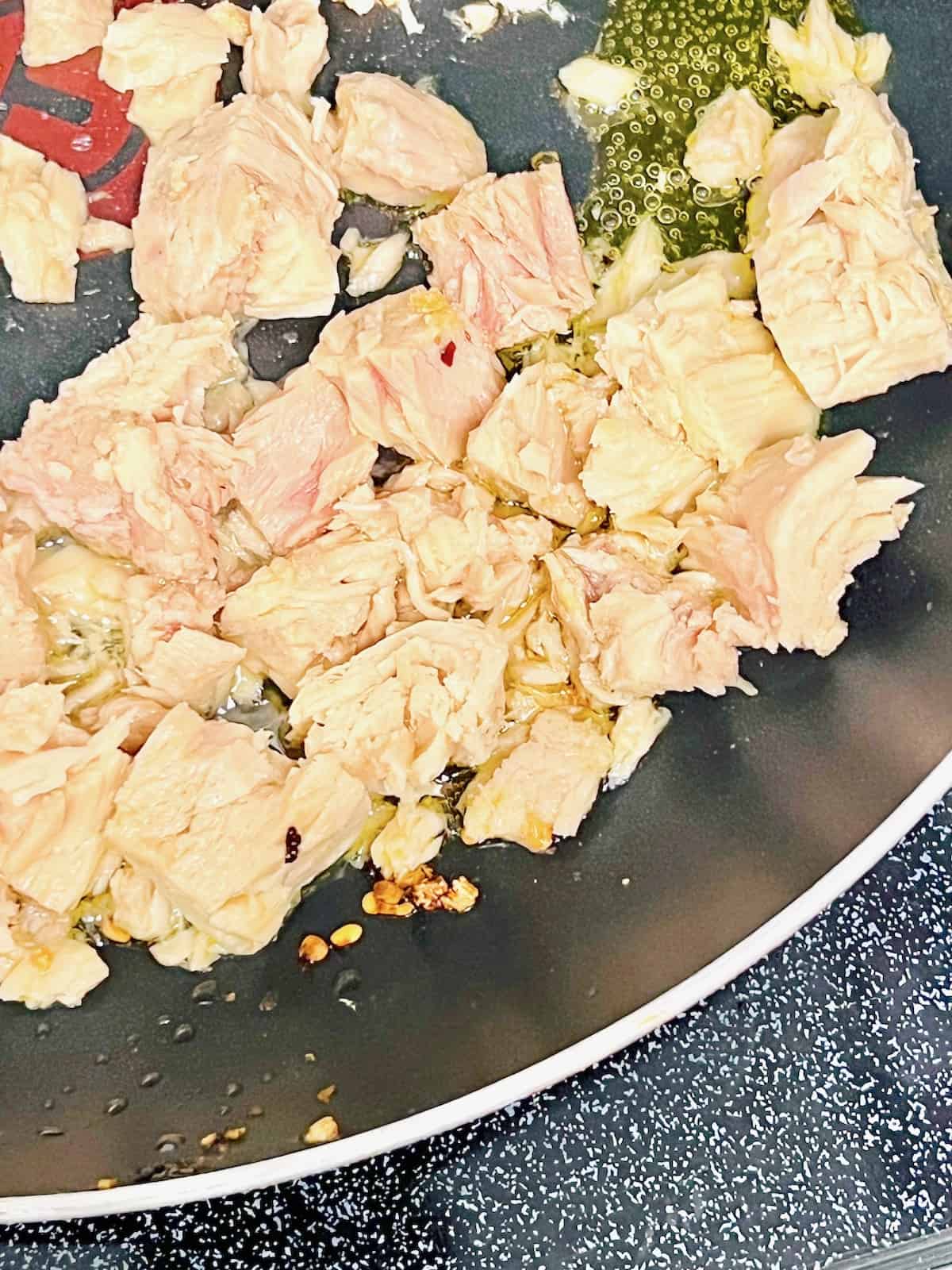 Adding canned tuna to the infused olive oil in a skillet.