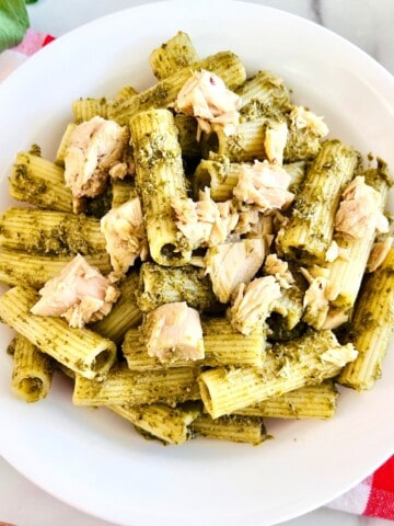 Simple pesto pasta with canned tuna in a bowl with red checkered napkin.