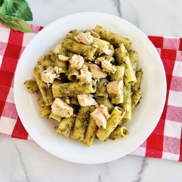 Pesto Tuna Pasta in a bowl with a red checkered napkin and fresh basil leaves to the side.