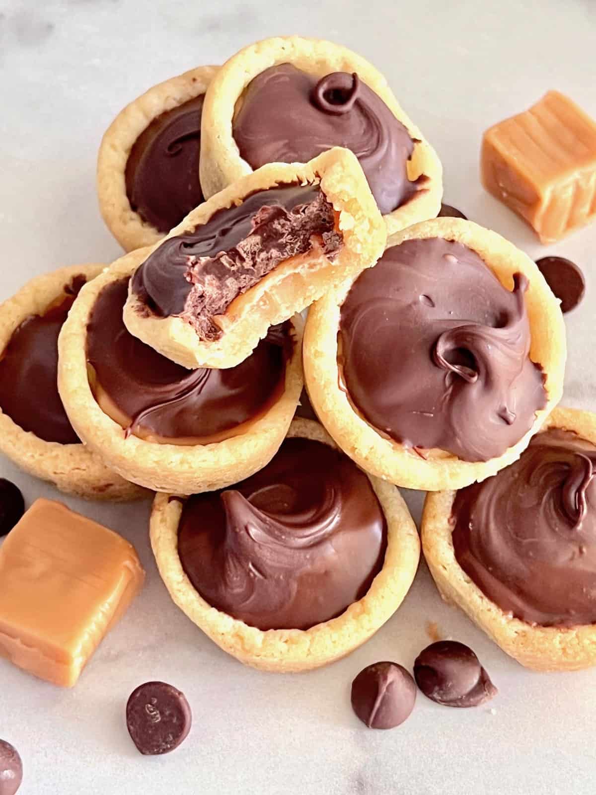 Twix Cookie Cups In a pile with one bitten plus chips and caramels on the side.
