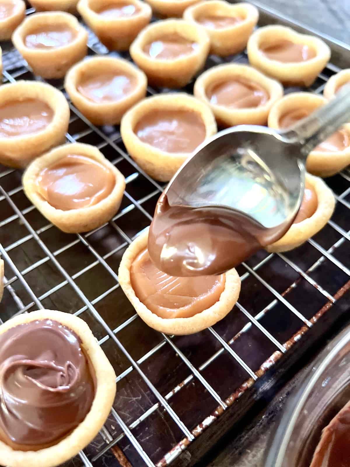 Twix Cookie Cups Spooning on melted chocolate to top the caramel layer.