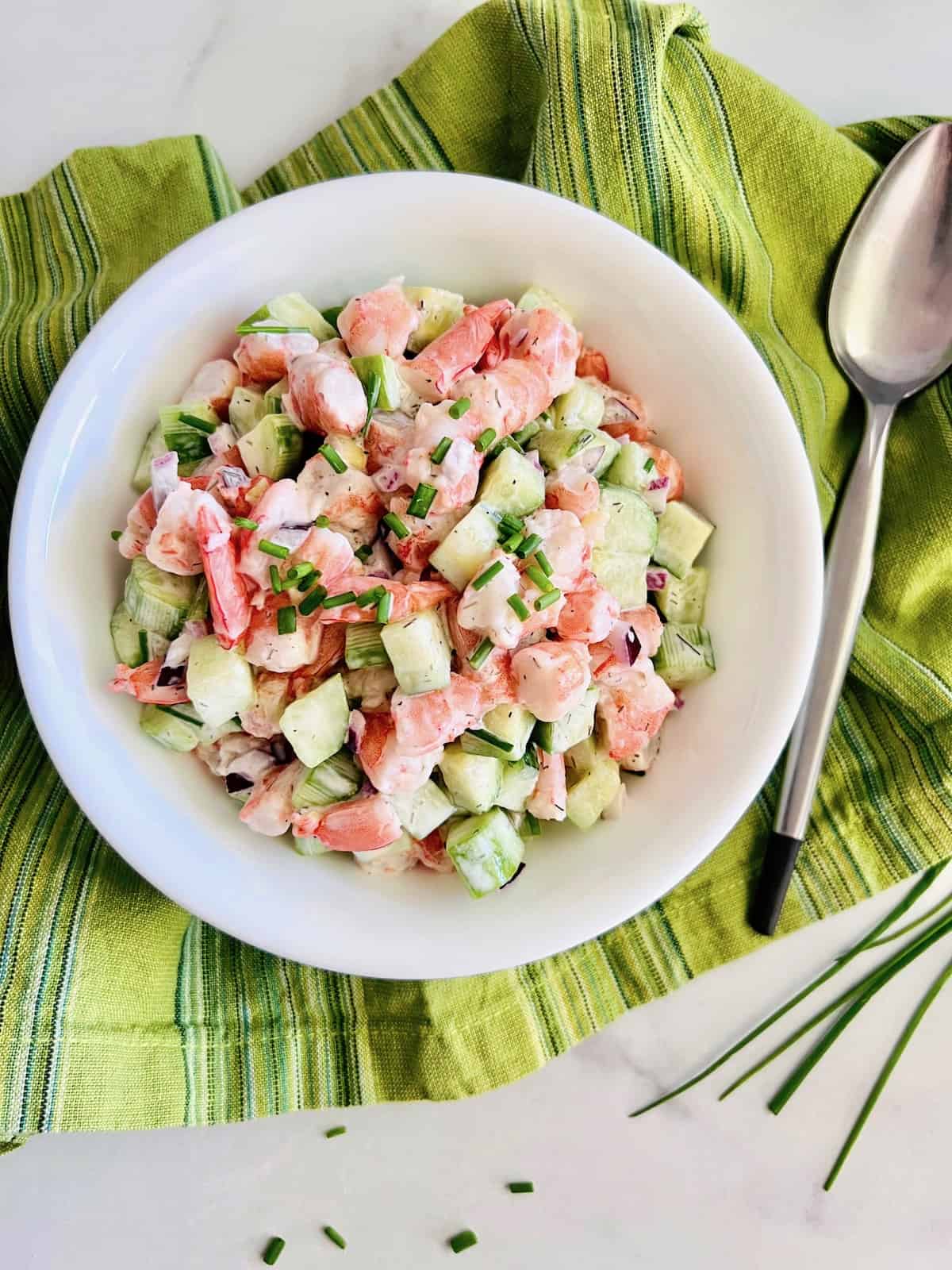 Cucumber Shrimp Salad In a white bowl with green napkin and spoon.