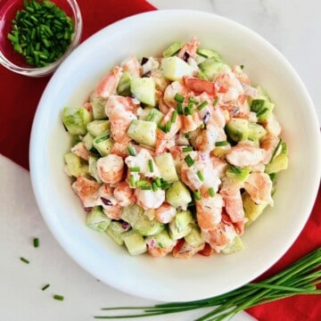 Ready to eat cucumber shrimp salad in a serving bowl dressed with a sour cream mayo dill dressing & topped with chives.