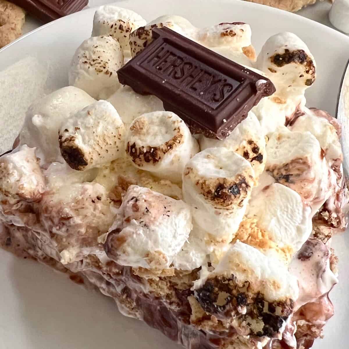 S'mores Icebox Cake square piece on a plate with toasty marshmallows & a hershey square on top.