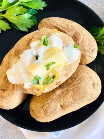 Plate piled with baked potatoes made in the air fryer and the top one is split open topped with butter and sour cream.