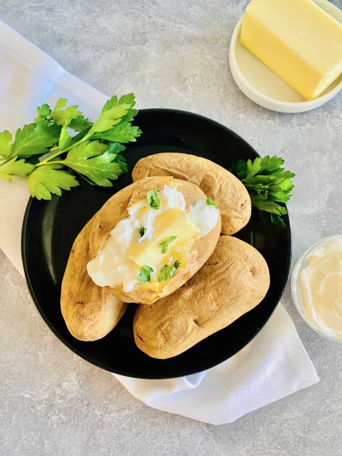 Air Fryer Baked Potatoes Topped with butter sour cream & fresh parsley on a plate.