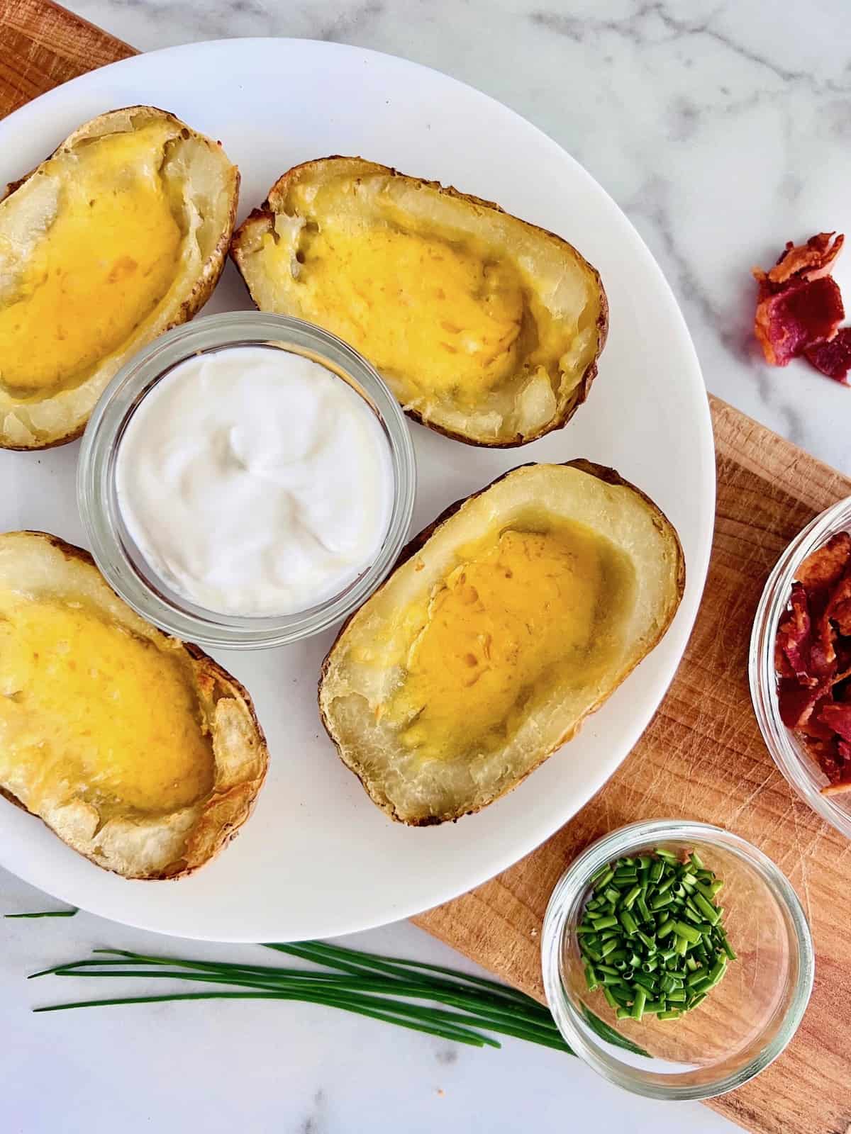 Crispy potato skins filled with melted cheddar next to bowls of toppings.
