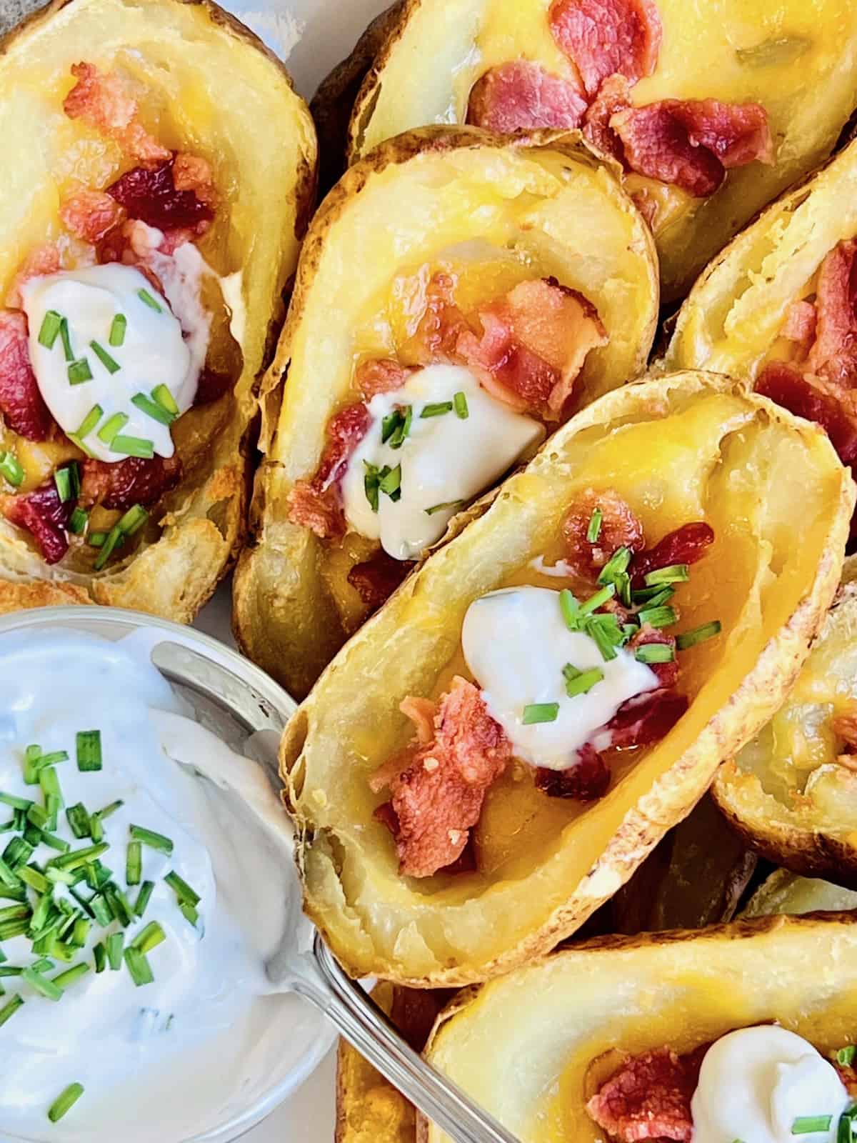 Air Fryer Loaded Potato Skins Fanned out on a plate with bowl or sour cream topped with fresh chives.