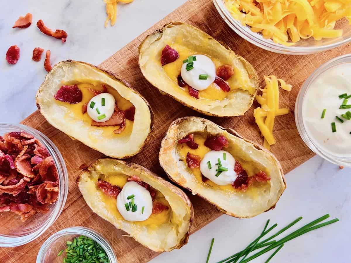 Potato skins stuffed with cheddar and bacon on a cutting board for a buffet with bowls of toppings