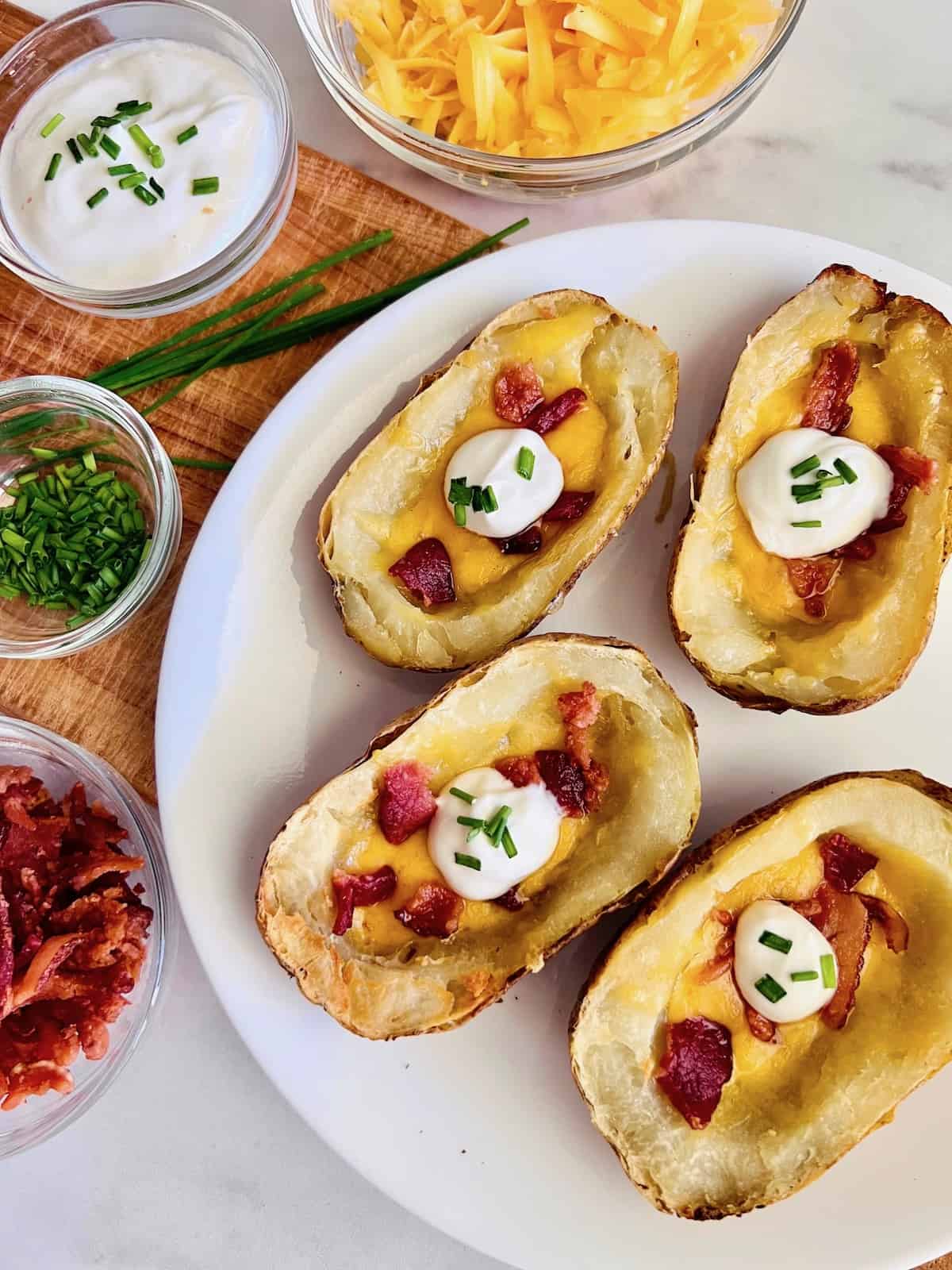 Air Fryer Loaded Potato Skins Surrounded by bowls of topping ingredients like bacon cheddar chives and sour cream,