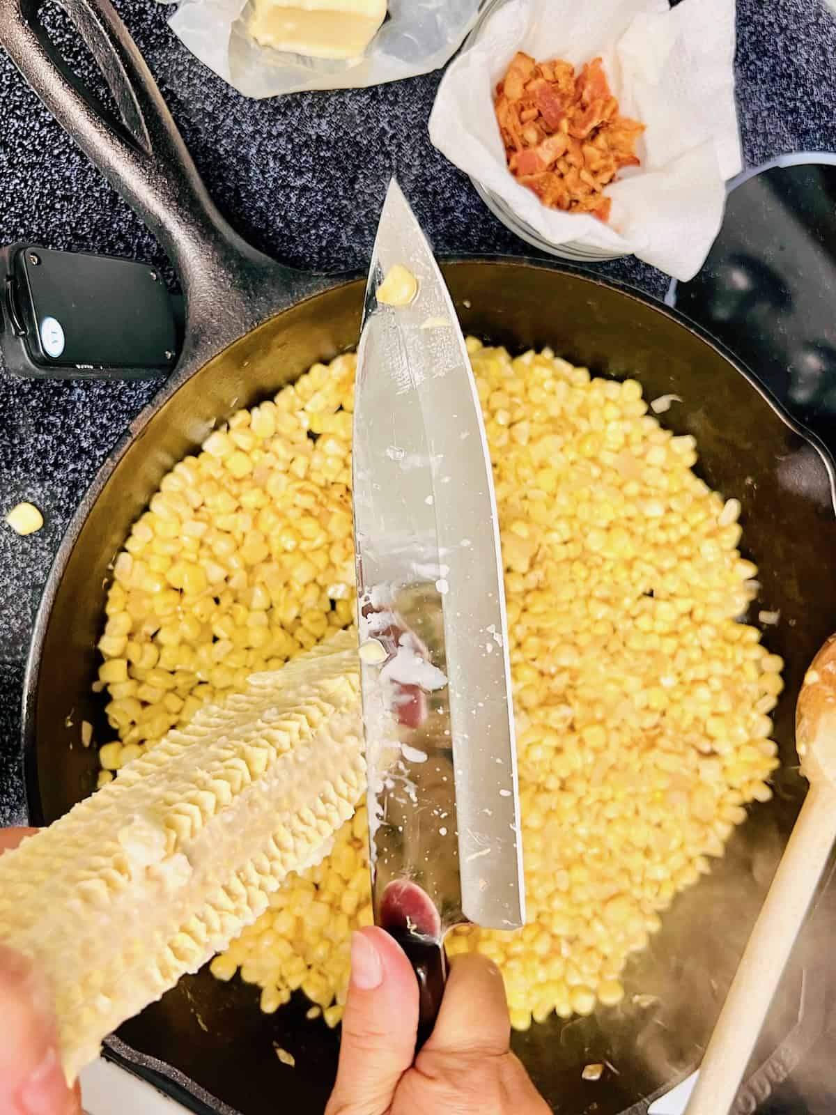 Scraping corn cobs without the kernels with the backend of chefs knife over a pan.