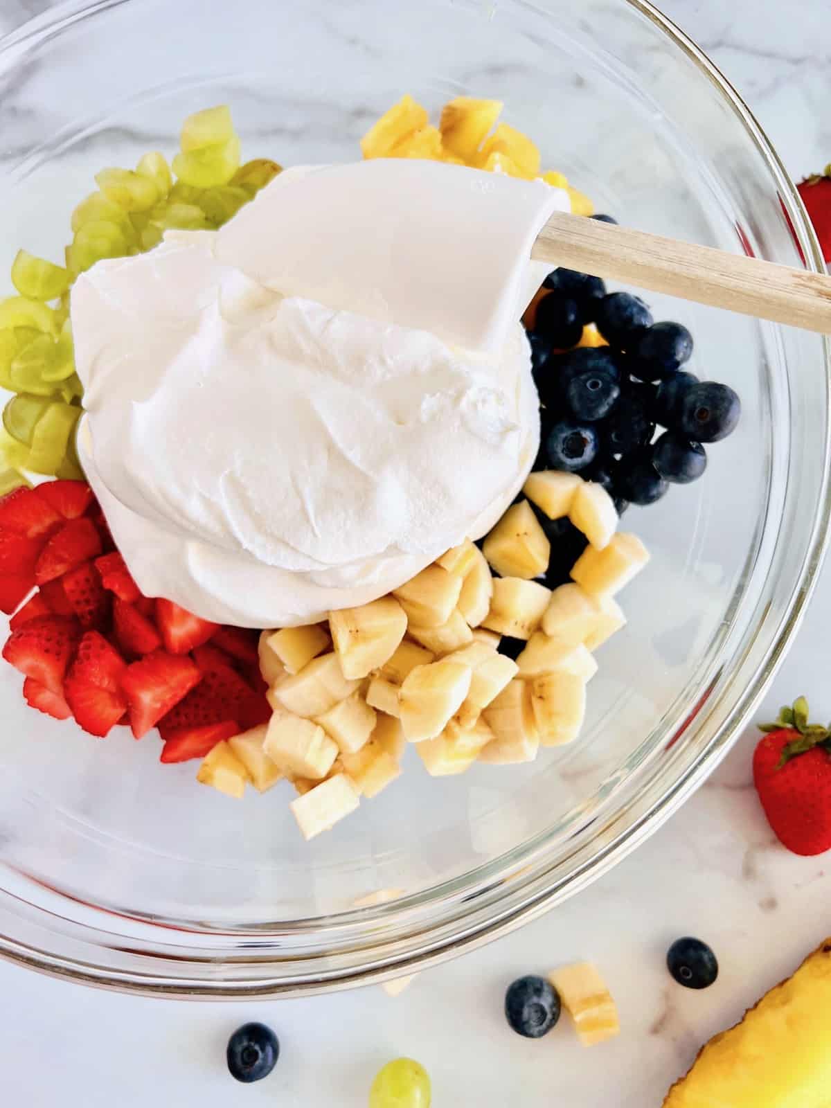 Scooping whipped topping onto cut fresh fruit.