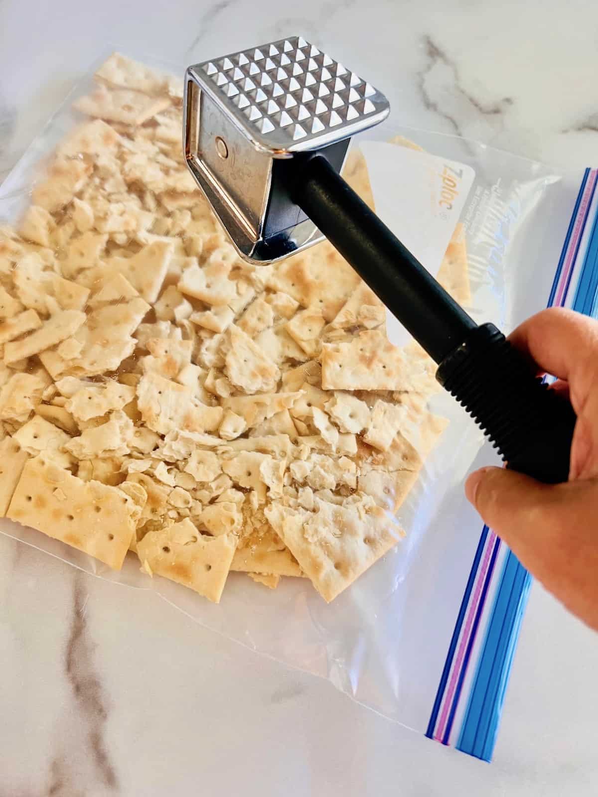 Ziploc bag filled with saltine crackers being crushed with kitchen mallet.