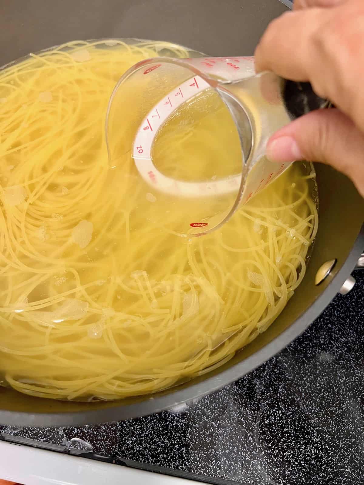 Measuring cup scooping pasta water.