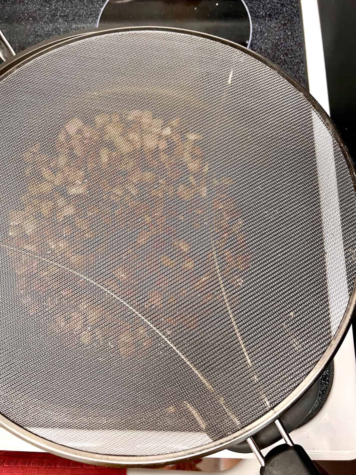 splatter screen over the pancetta cooking in a pan