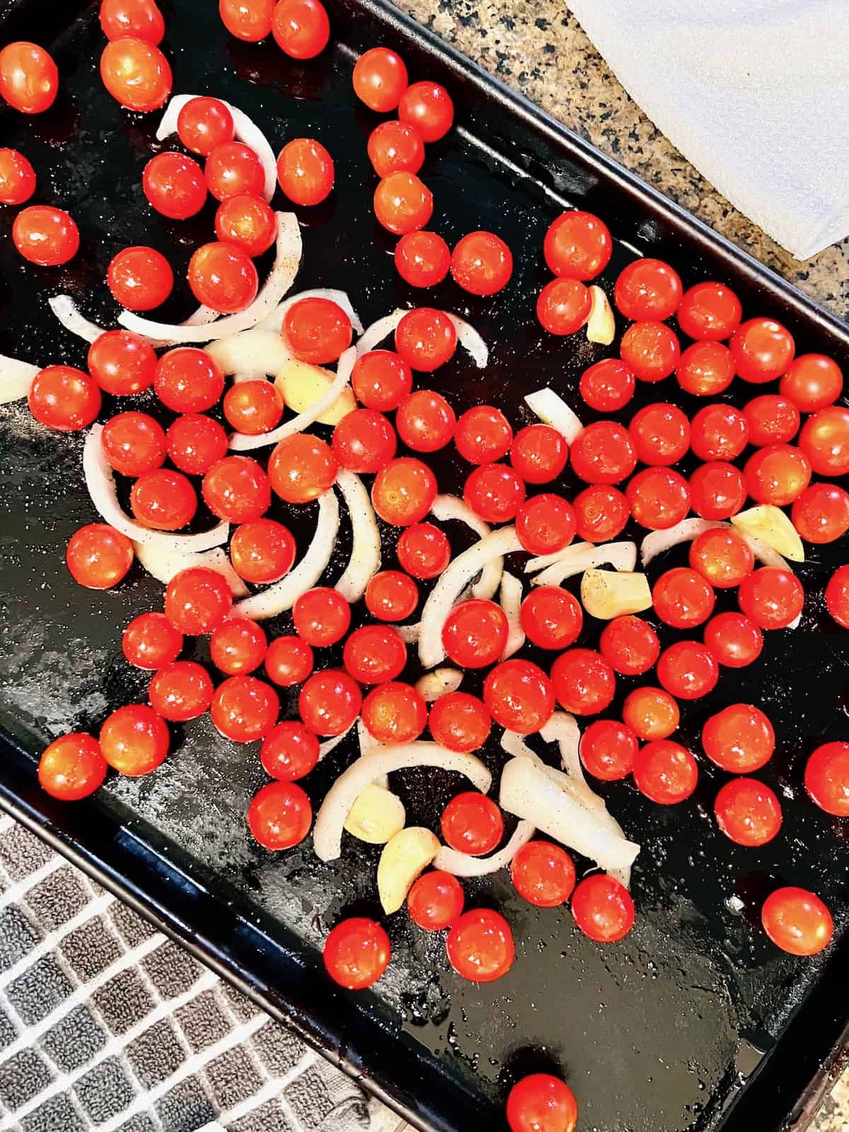 Baking sheet with garlic onion cherry tomatoes in olive oil.