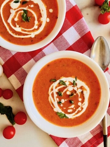 Roasted Cherry Tomato Soup bowls ready to eat with a spoon & on the table with fresh basil & napkin.