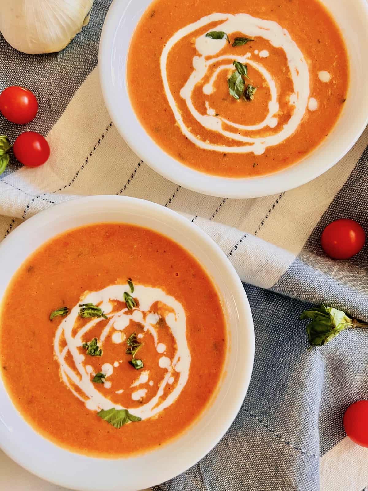 Roasted Cherry Tomato Soup Overhead two bowls with swirled cream and basil leaves on grey white linen napkin.