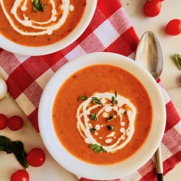 Two bowls of homemade soup made with cherry tomatoes basil and cream.