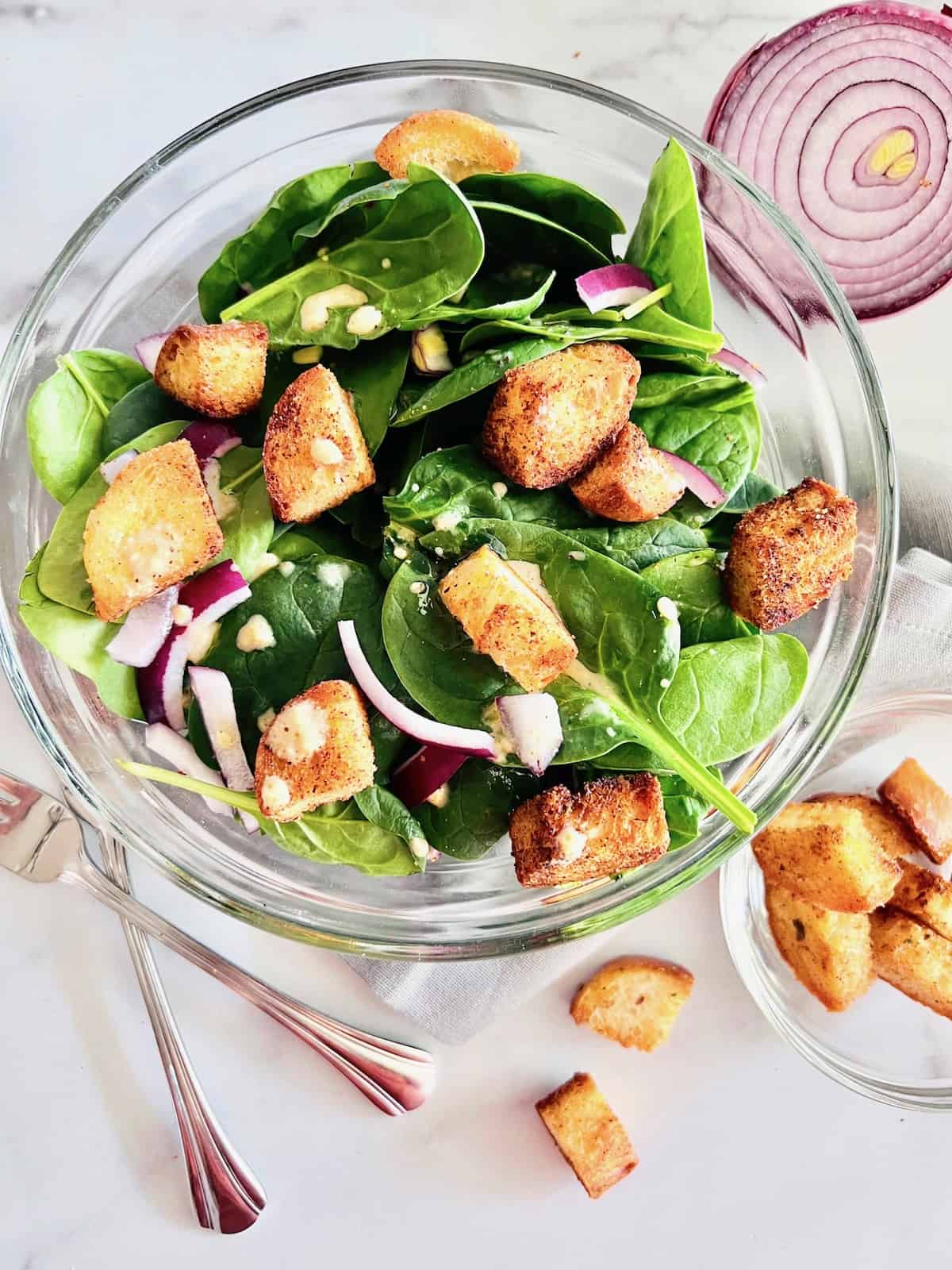 Simple Spinach Salad Glass bowl filled and ready to serve with fork red onion and croutons on the side.