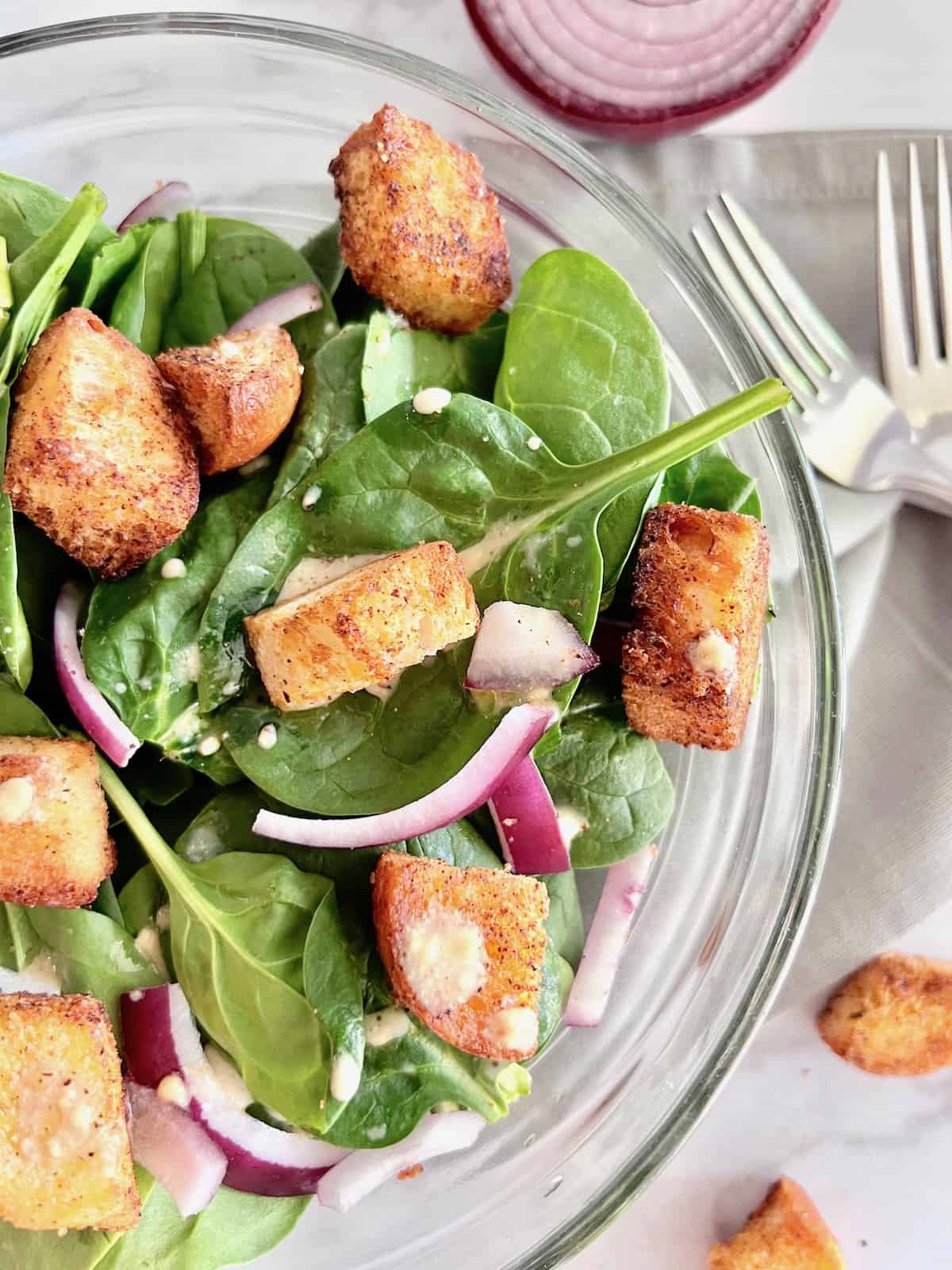 Easy & basic Spinach Salad Overhead of half glass bowl with spinach salad topped with croutons and dijon vinaigrette