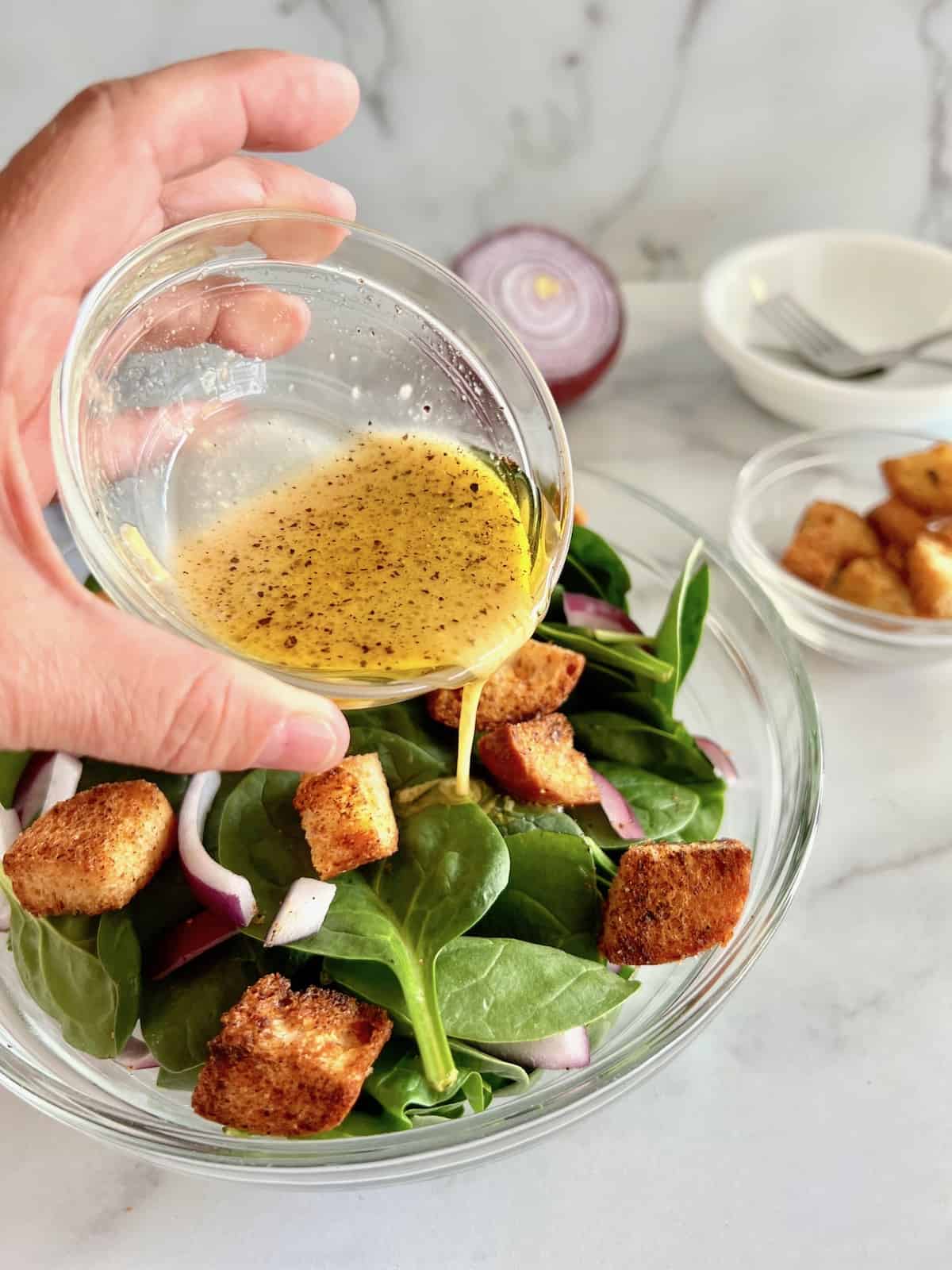 Pouring the dijon vinaigrette on the bowl of spinach salad.
