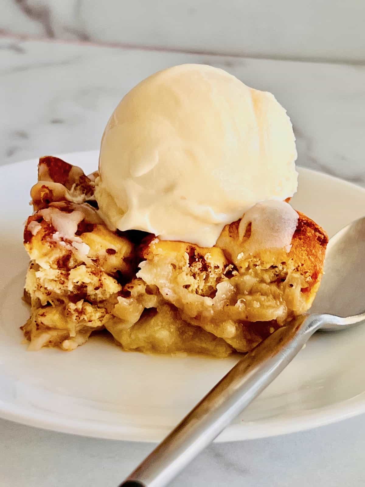 Cinnamon Roll Peach Cobbler plated with an Ice Cream Scoop on top of a slice.