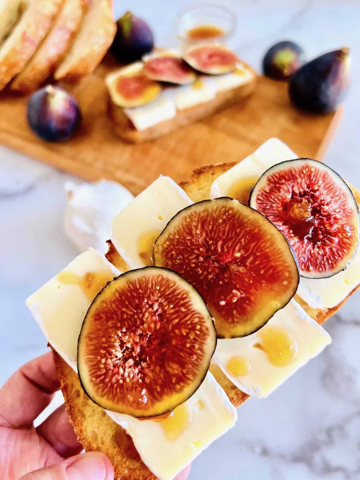 Holding one close up to show drizzled honey over figs and brie on toasted bread.