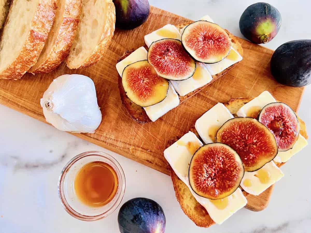 Cutting board with two bruschetta toasts topped with sliced figs and  brie.