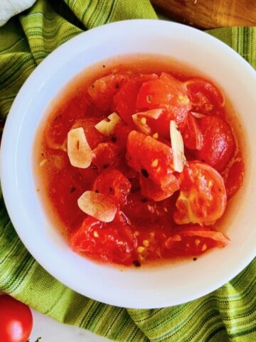White bowl of italian marinated tomatoes with garlic and oregano.