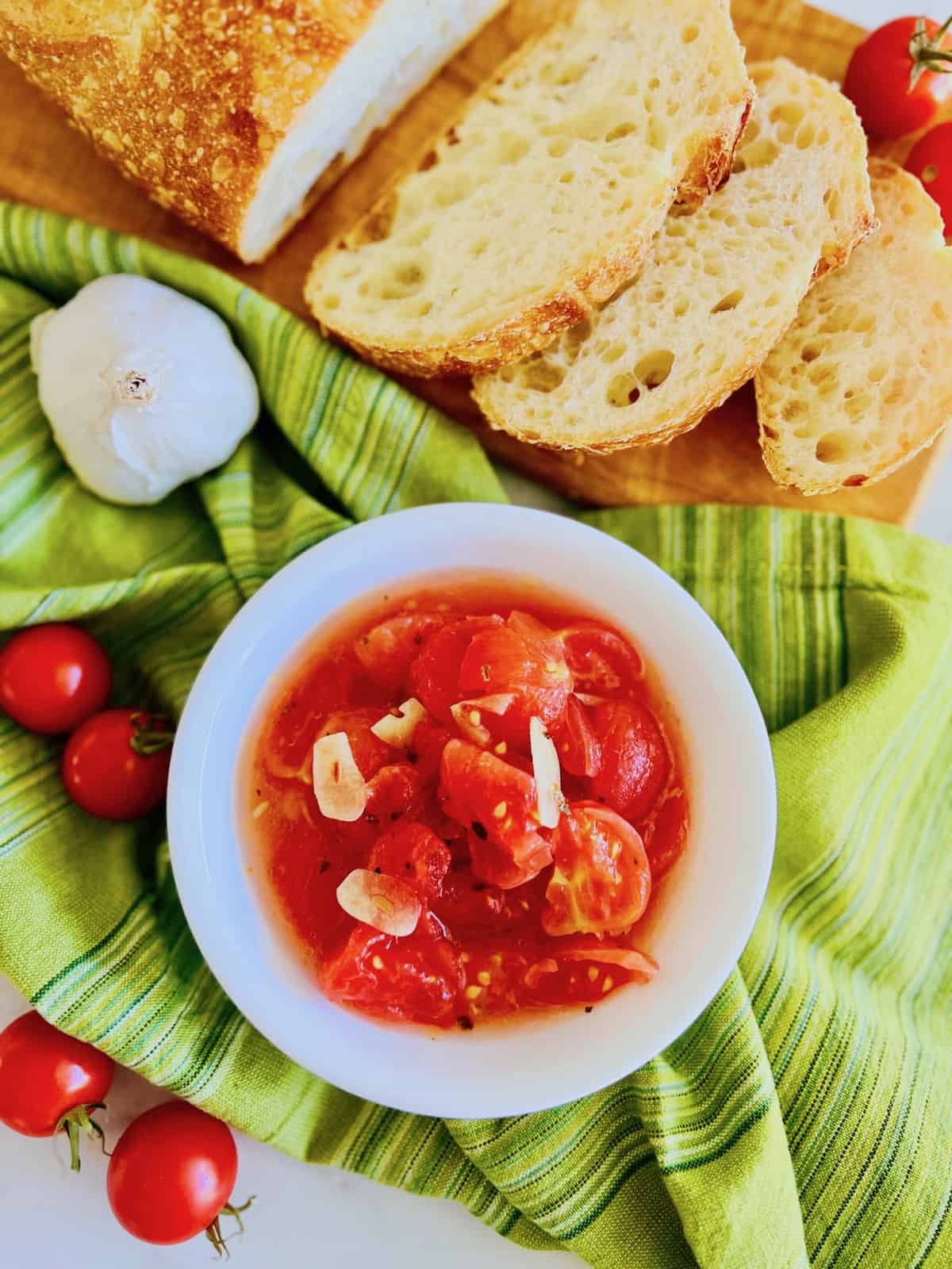 Italian Marinated Tomatoes Overhead bowl plus sliced bread green napkin tomatoes and garlic.