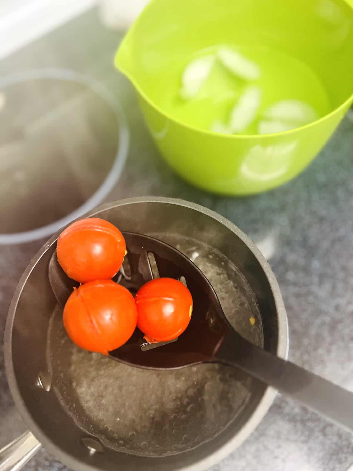 Slotted spoon lifting blanched tomatoes out of simmer pot of water.