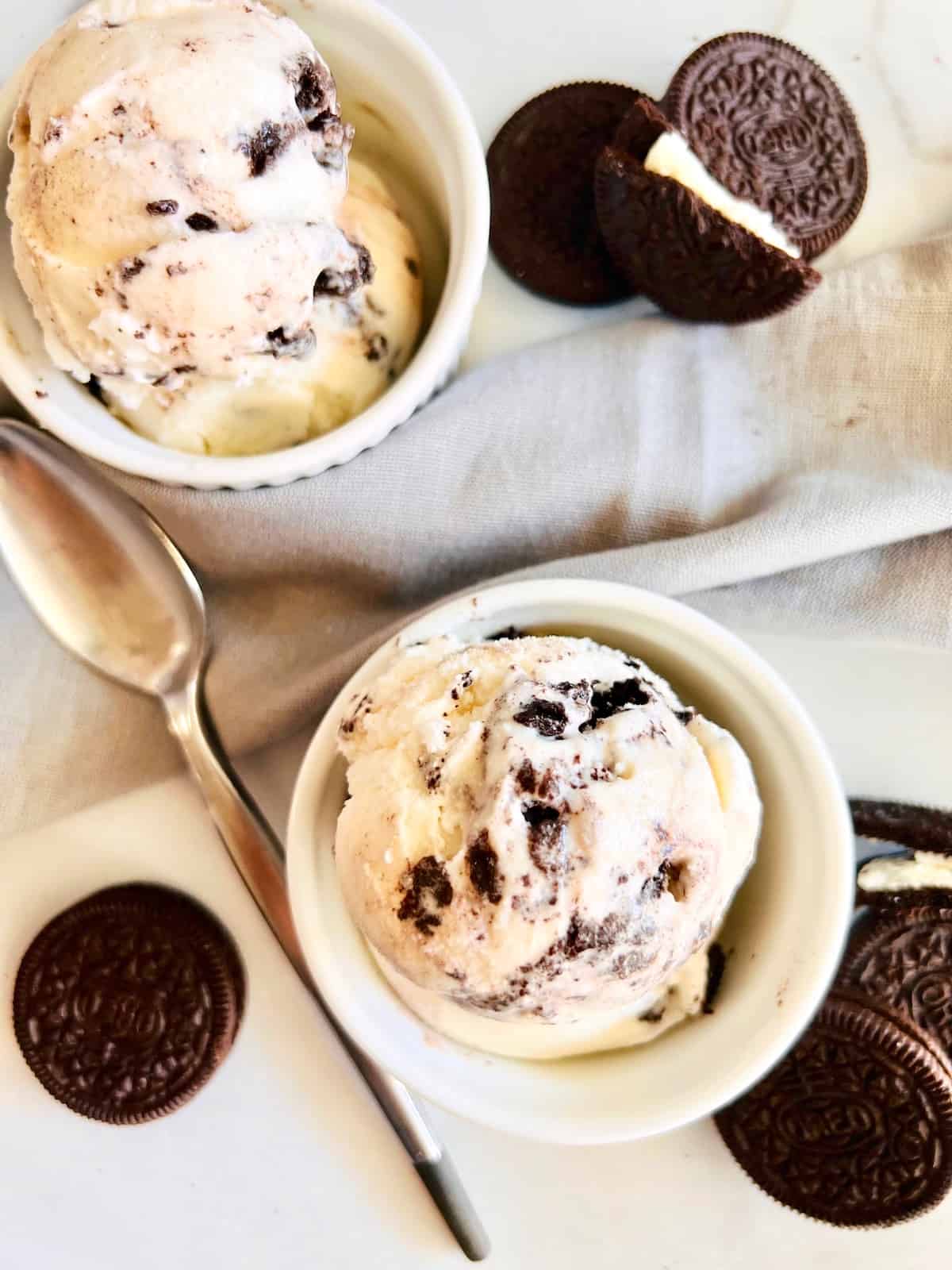 Vanilla ice cream with Oreo cookies made from scratch served in white dishes next to sandwich cookies and spoon.