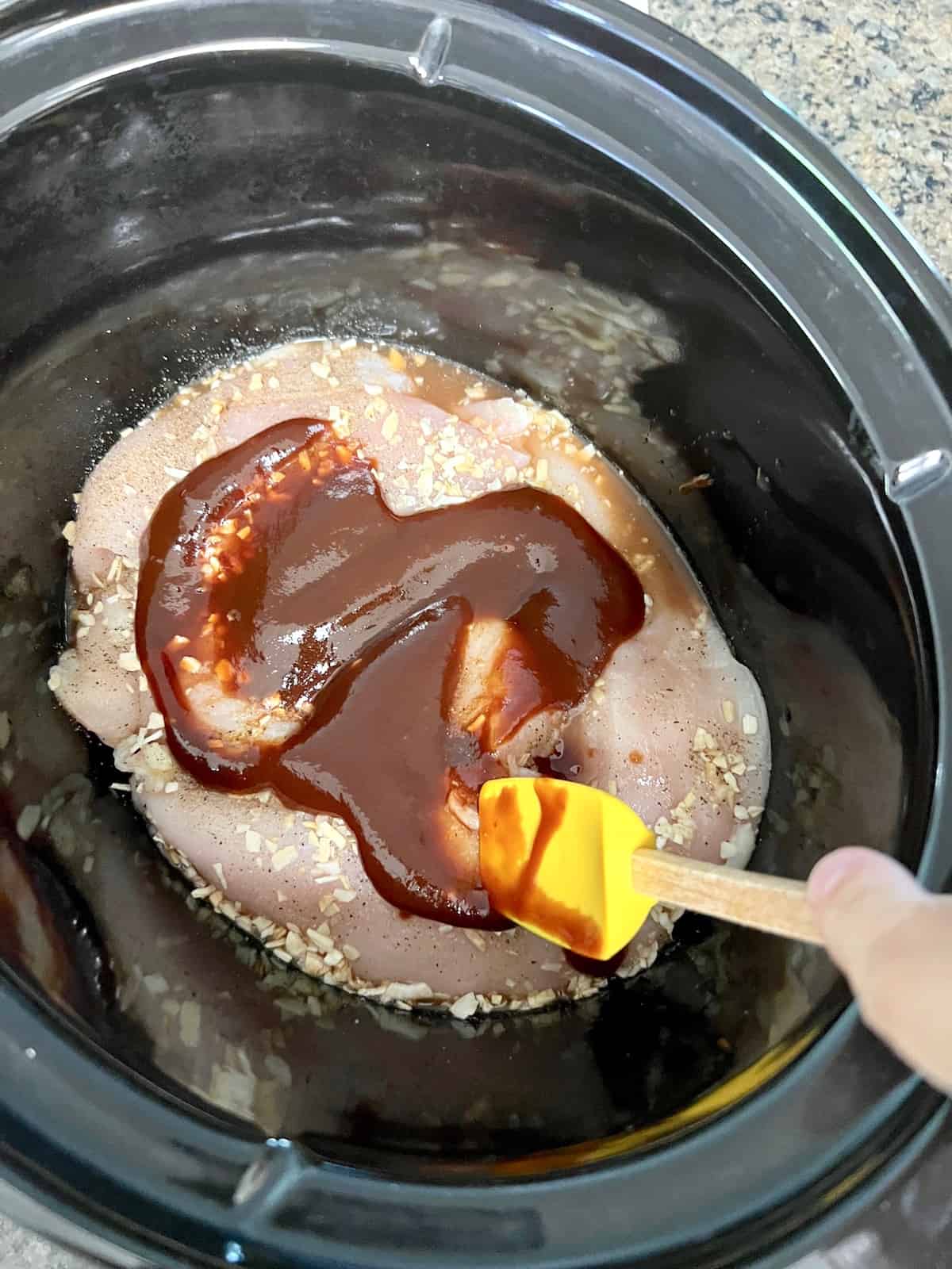 Adding ingredients and spreading bbq sauce over raw chicken.