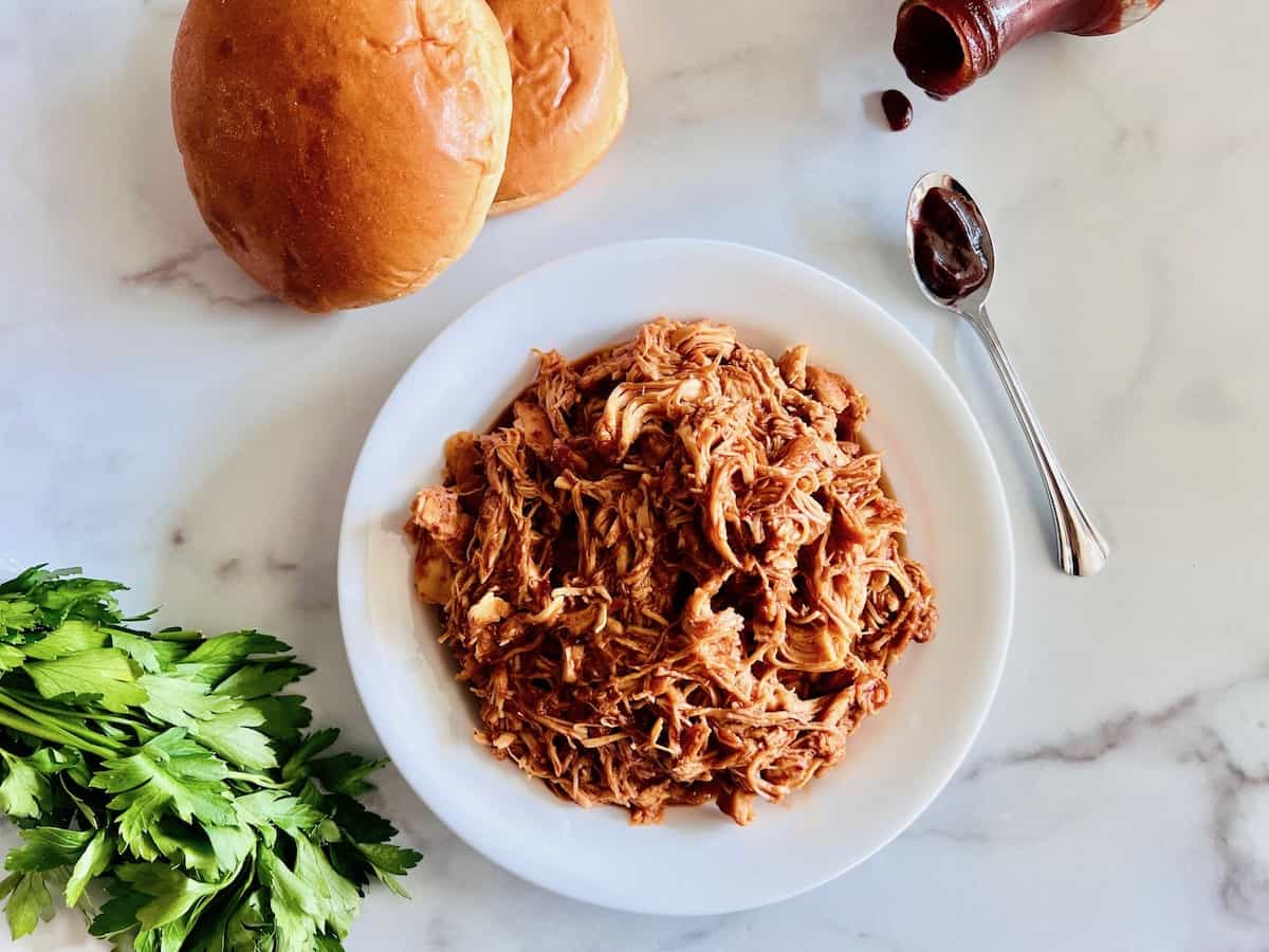 Slow Cooker BBQ Pulled Chicken in a bowl ready to serve on buns with extra barbecue sauce. 