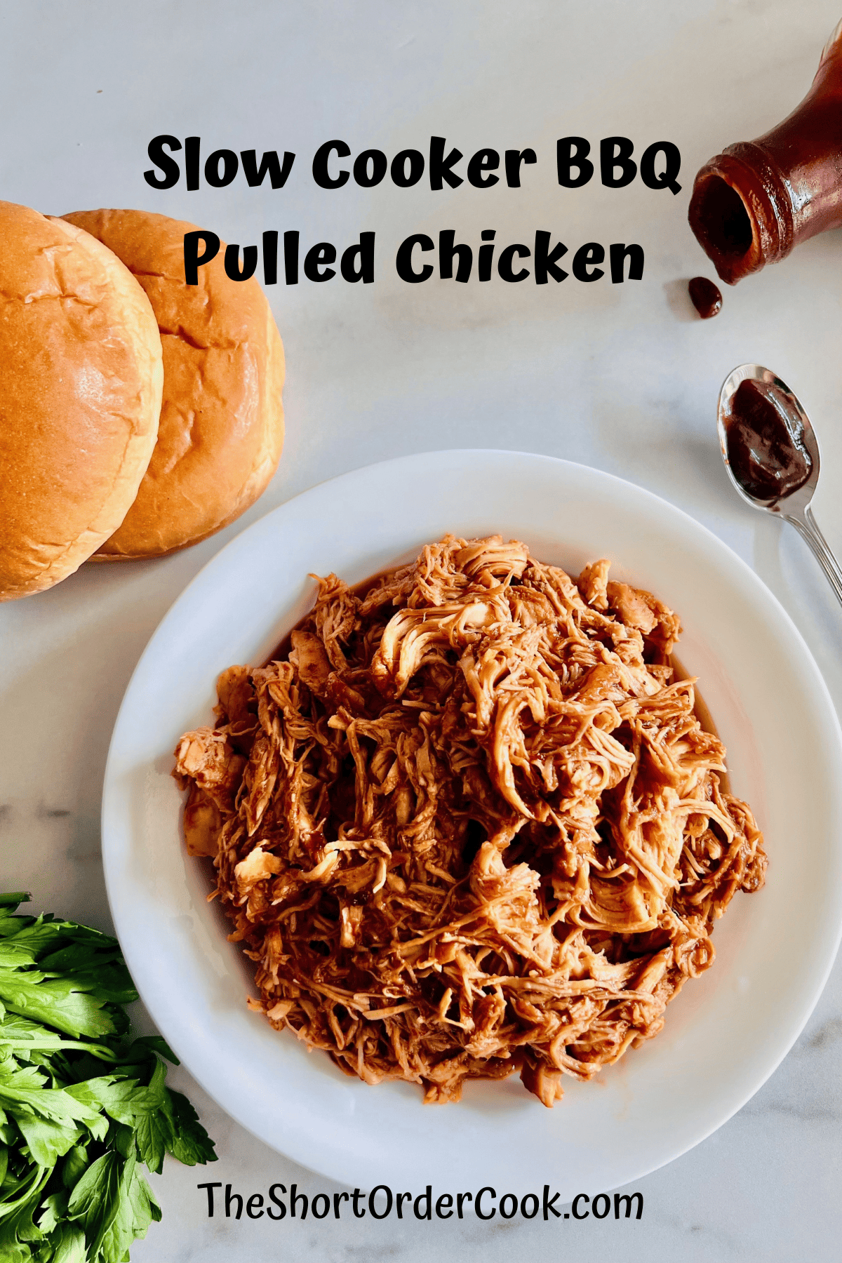 Slow Cooker BBQ Pulled Chicken in a bowl ready to serve next to hamburger buns, bbq sauce, & fresh parsley.